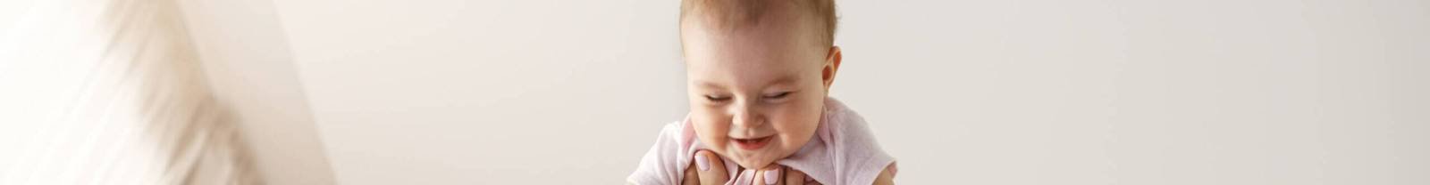 Young cheerful mother playing with her newborn baby lying on bed at home. Copy space.